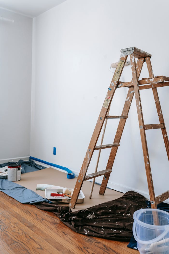 A home renovation scene featuring a wooden ladder, painting tools, and white walls in a room.